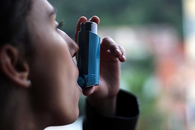 Junge Frau sprüht sich sich ein Asthma-Spray.